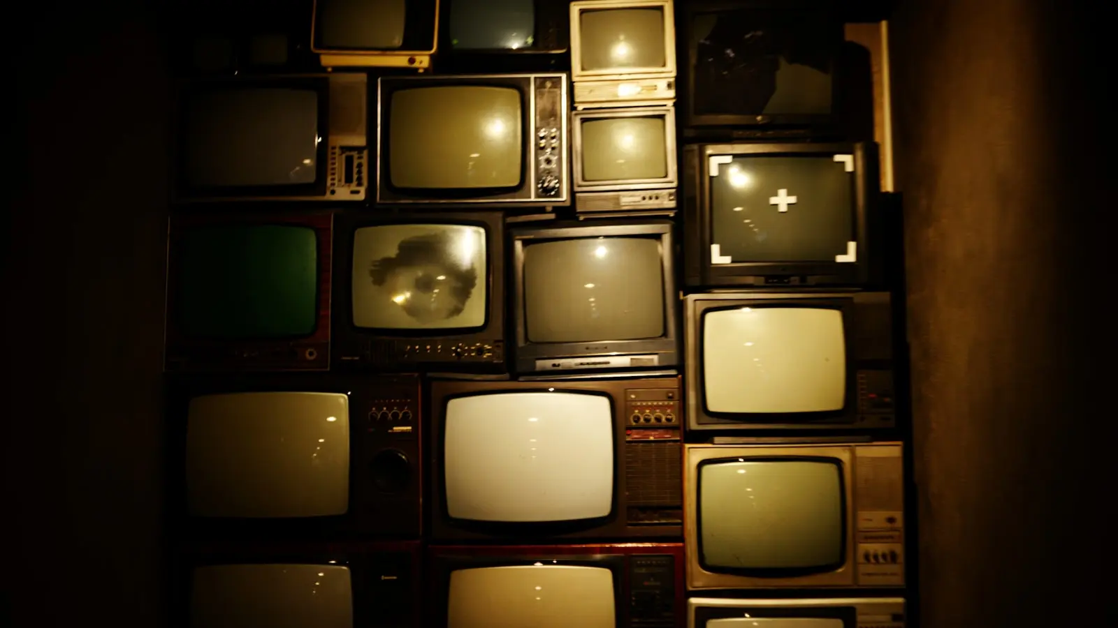 Mur de téléviseurs vintage dans une pièce sombre — la télé « standard » face au premium